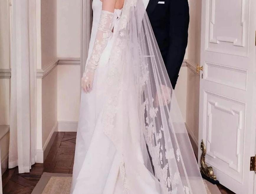 Nicola Peltz in her white gown and cascading veil and Brooklyn Beckham in his black tuxedo posing after their wedding ceremony.